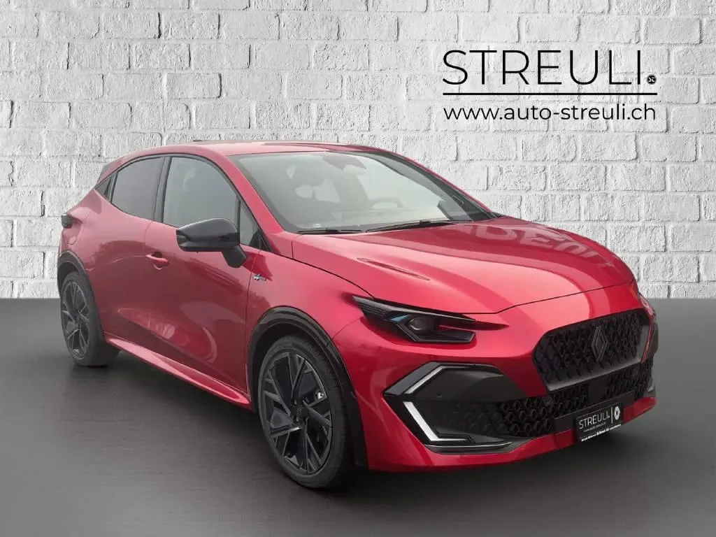 Schrägansicht von vorne links auf einen roten Renault Clio E-Tech esprit Alpine vor einer weissen Ziegelwand.