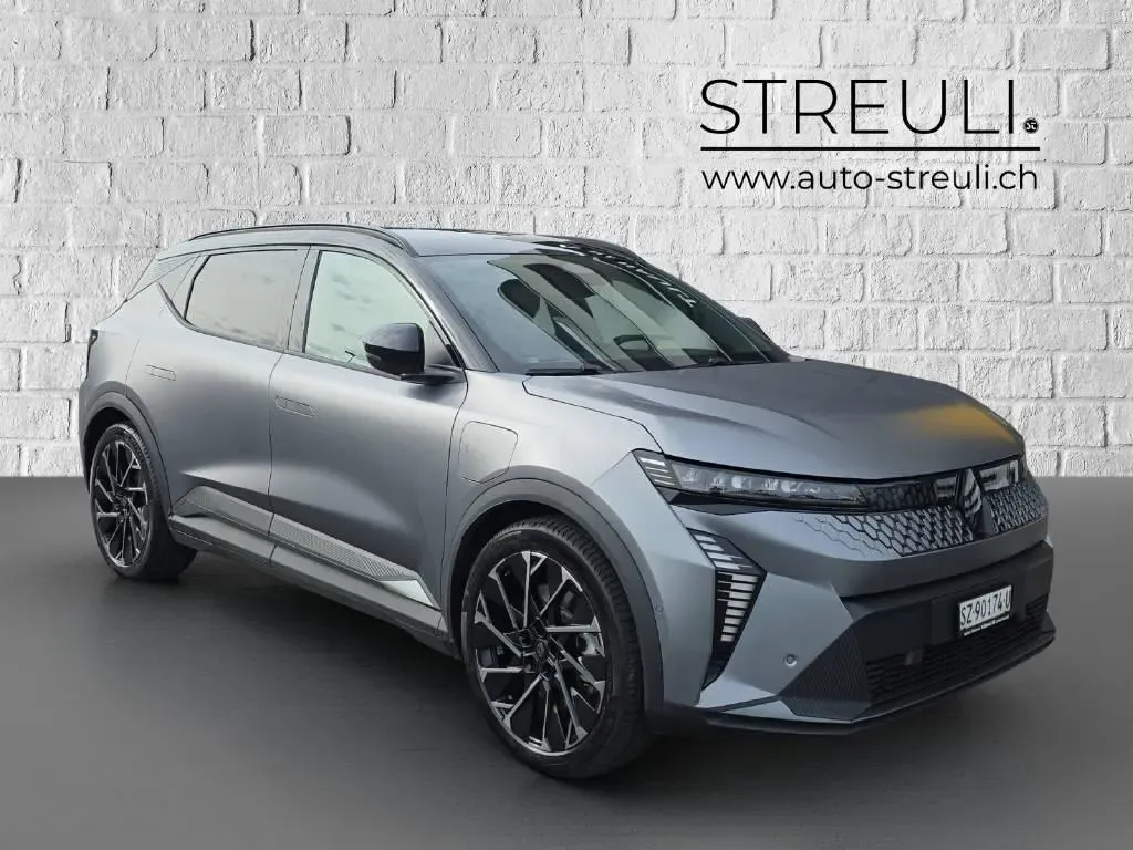 Schräge Frontansicht eines grauen Renault Scenic E-Tech Esprit Alpine vor einer weissen Ziegelwand.