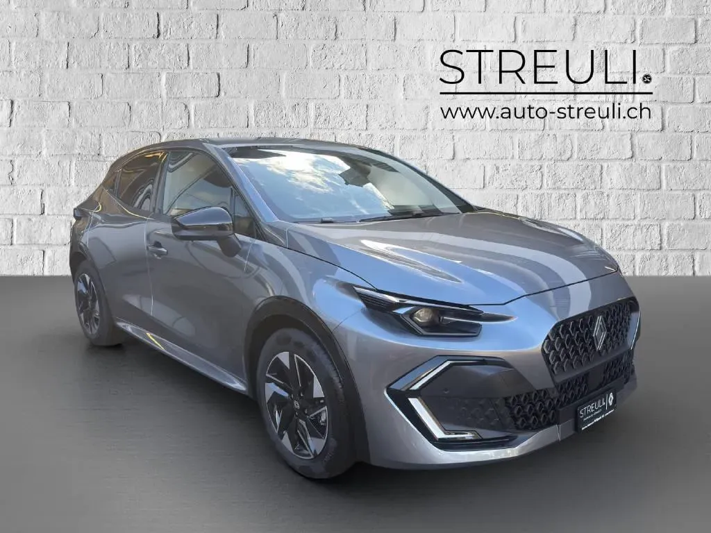 Schräge Frontansicht eines grauen Renault Clio E-Tech techno vor einer weissen Backsteinwand.
